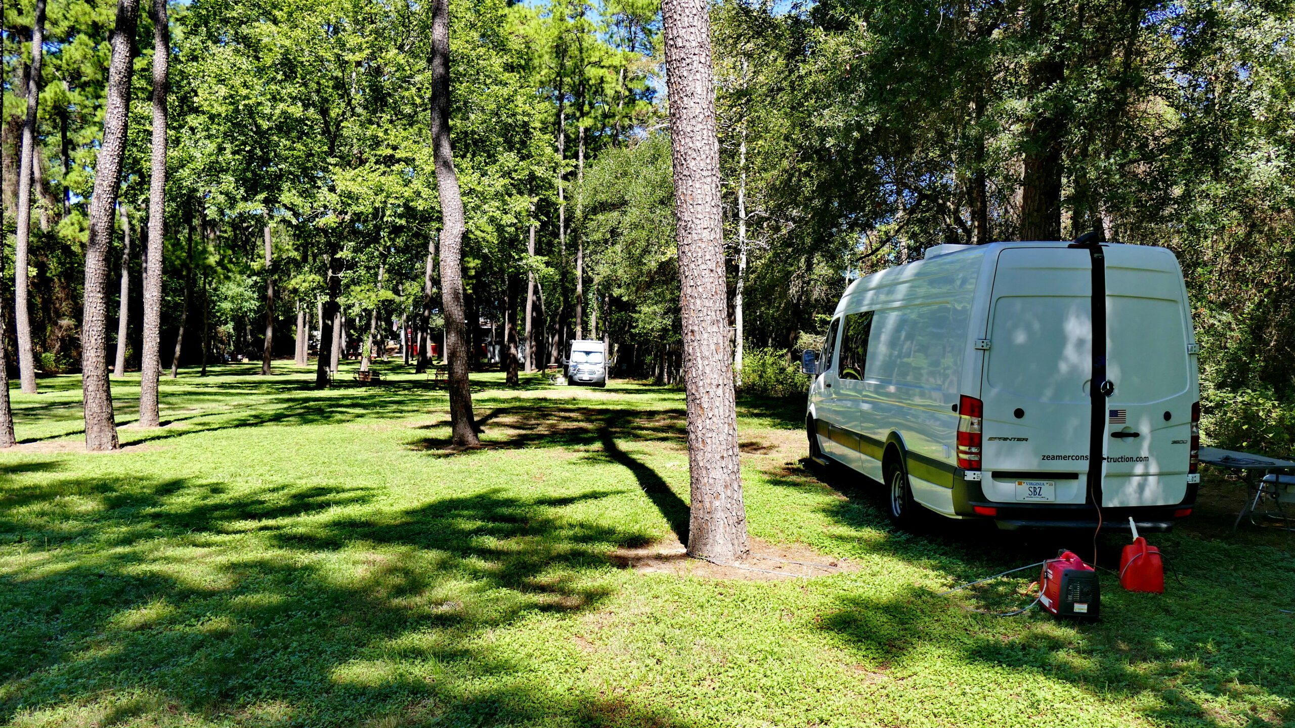 RV's and Tents scattered across a grassy field under starry night sky, with campfire in the foreground"